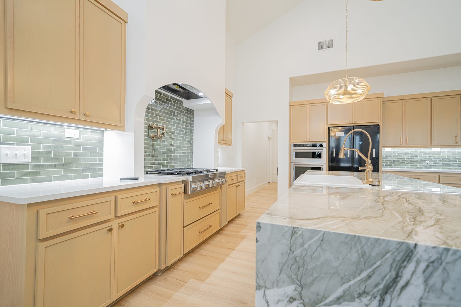Kitchen with natural wood cabinets, green tile backsplash and a marble waterfall island