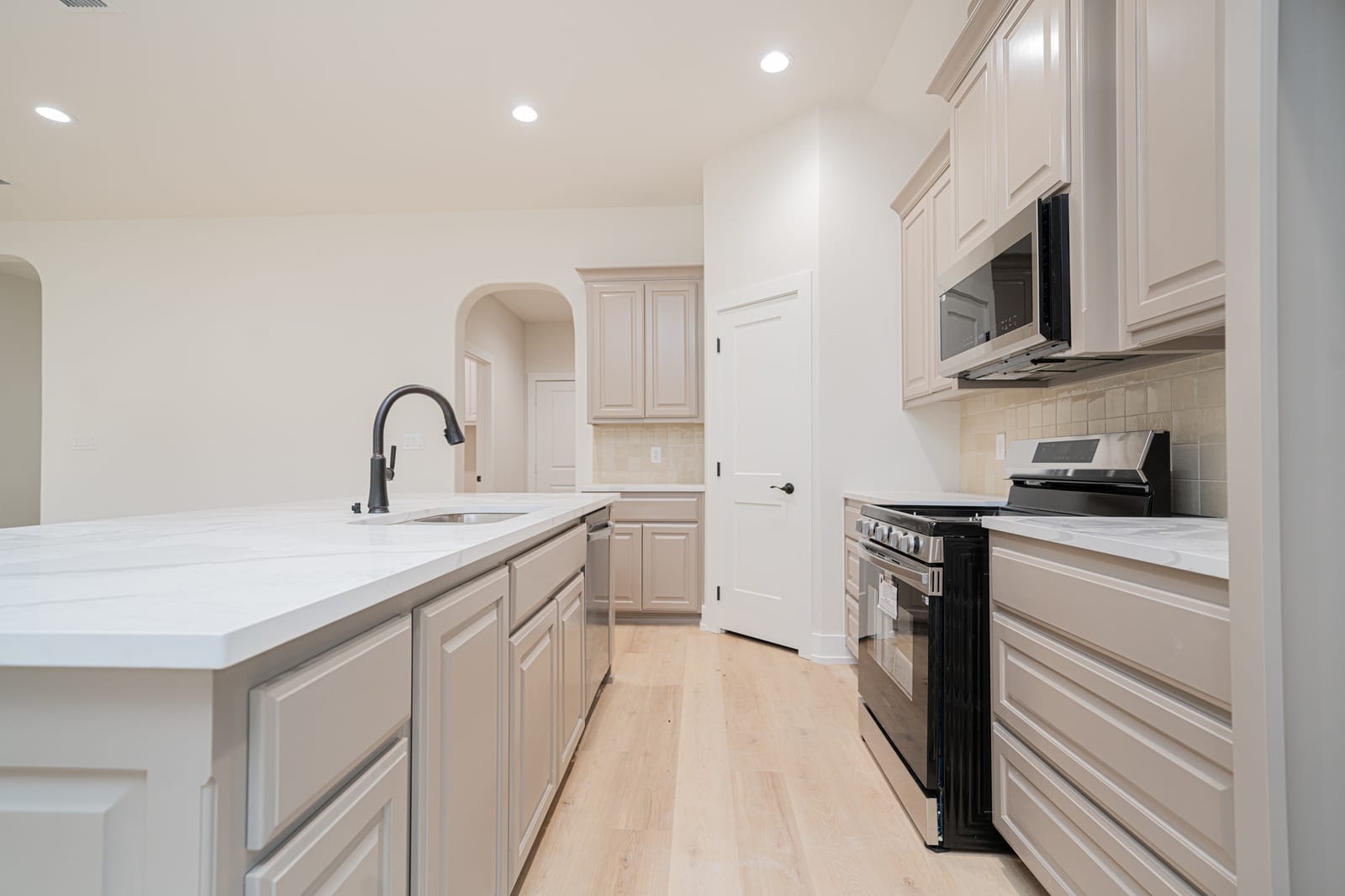 Kitchen with greige cabinets, a white stone island and stainless range