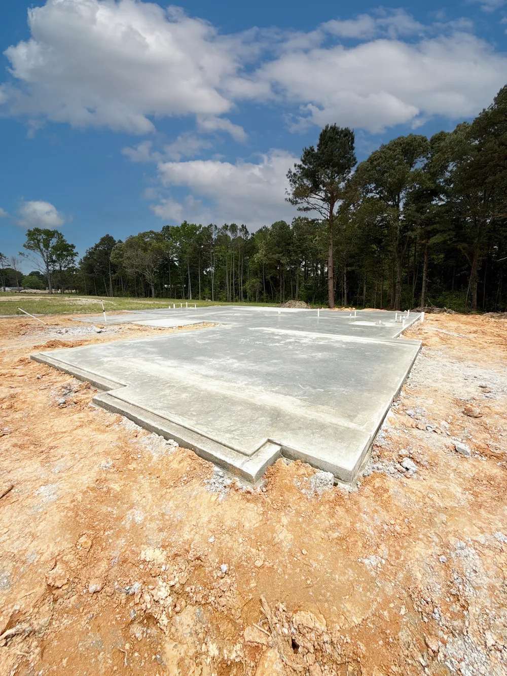 Poured concrete foundation slab on a cleared homesite with pine trees behind